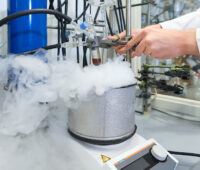 Im chemischen Labor steht ein dampfender Topf auf einem Kochfeld. Ein wissenschaftler experimentiert mit einer dunklen Flüssigkeit in einem Reagenzglas.