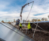 Solarthermie: Bauarbeiter bugsieren einen Großkollektor, der an einem Kran hängt, in seine Halterung