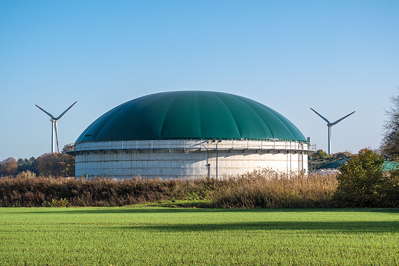 Biogasanlage in der Mitte, rechts und links im Hintergrund WIndkraftanlagen,