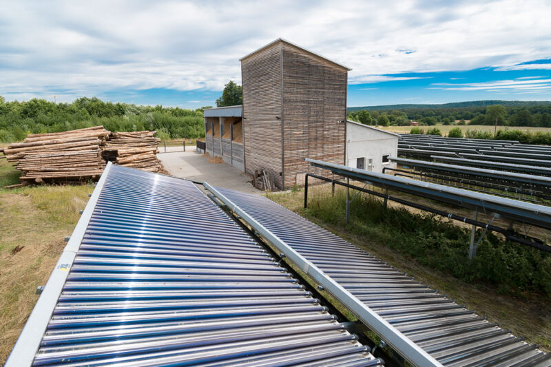 Holzheizwerk im Hintergrund, im Vordergrund: Solarthermieanlage. Symbolbild für sparsame Bioenergienutzung laut Biomassestrategie