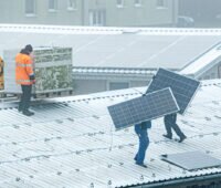 Arbeiter bauen eine Photovoltaikanlage auf eiem Dach wegen Qualitätsmängeln ab.