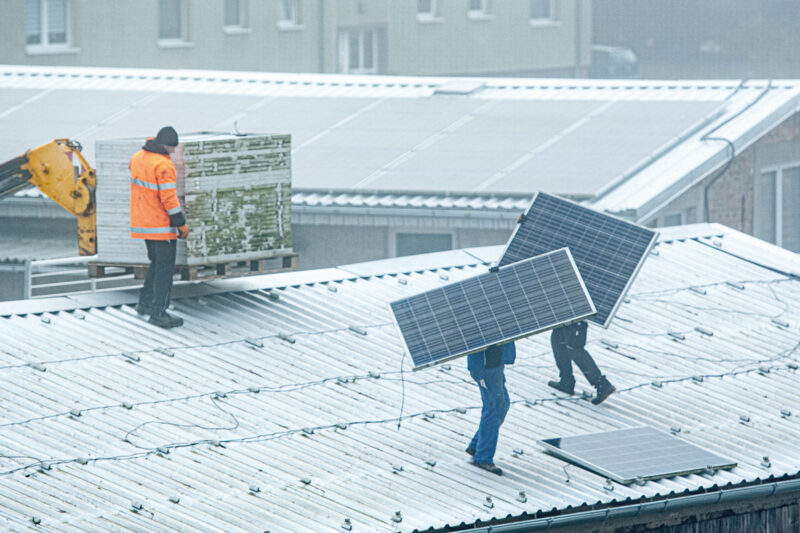 Arbeiter bauen eine Photovoltaikanlage auf eiem Dach wegen Qualitätsmängeln ab.