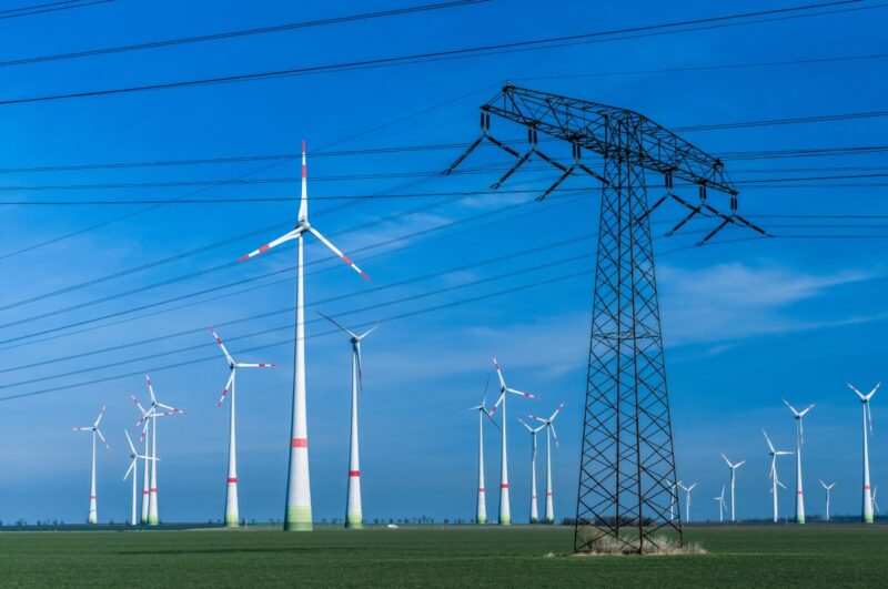 Windenergieanlagen neben Stromleitungen und Strommast.