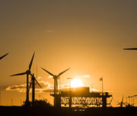 Bei untergehender Sonne Windkraftanlagen mit Industrieanlagen