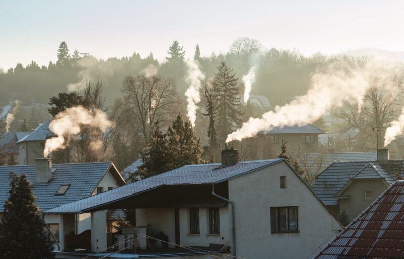 Ein Ortsbild mit Dächern. Aus vielen Schornsteinen steigt Qualm - Emissionen - auf.