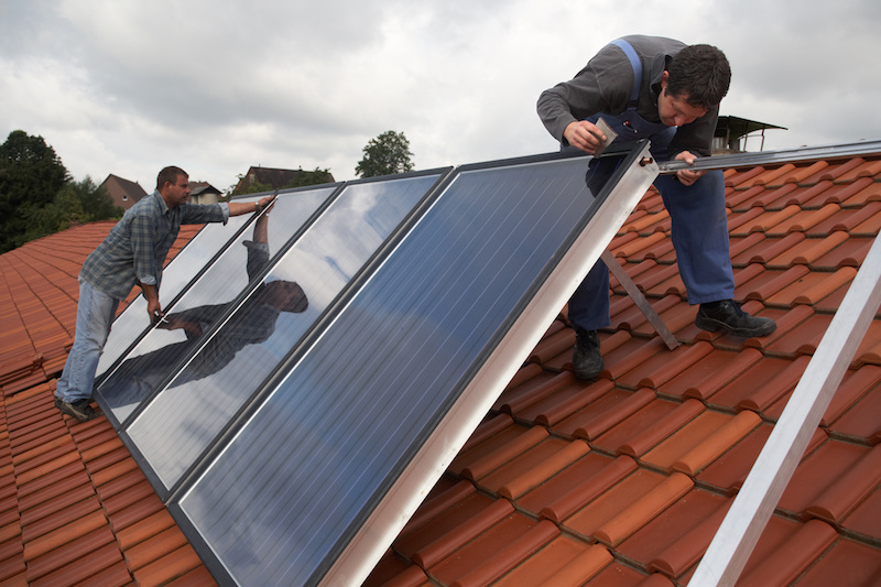 Zwei Installateure montieren Solarkollektoren einer Solarthermie-Anlage auf einem Dach.