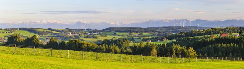 Bayerische bäuerliche Landwirtschaft, im Hintergrund die Alpen, rechts davor, kaum zu erkennen, ein Windpark