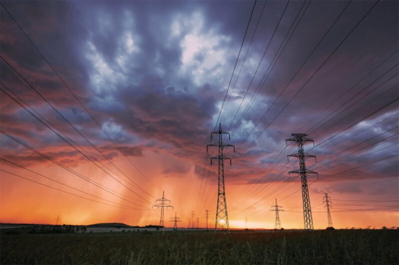 Sonnenuntergang und dunkle Wolken. Es ragen Strommasten empor.