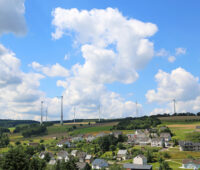 Im Vordergrund ein Dort im Hunsrück, im Hintergrund Windkraftanlagen mit akzeptierten Windkraft-Abständen
