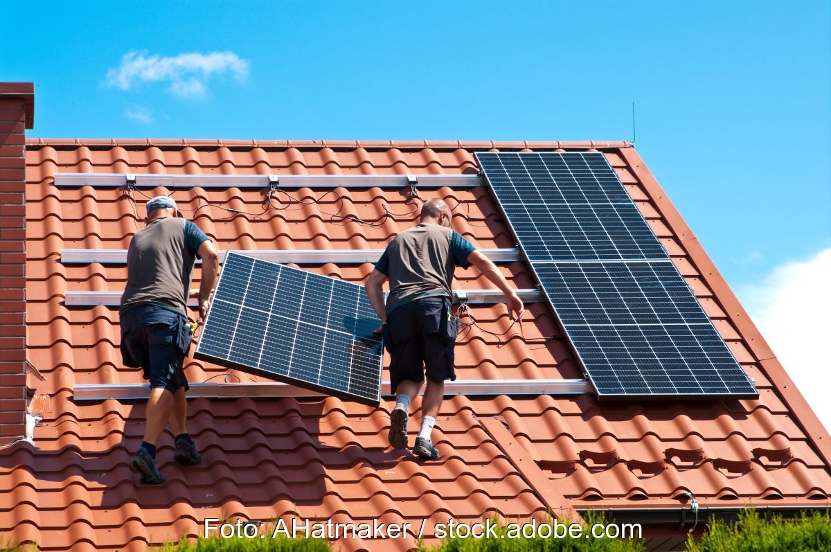 Zwei Monteure tragen PV-Modul auf ein Spitzdach.