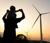 Vater mit Kind im Gegenlicht vor Windenergieanlagen bei Sonnenaufgang
