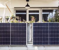 Zwei Solarmodule an einem mit Blumen bepflanzten Balkon.