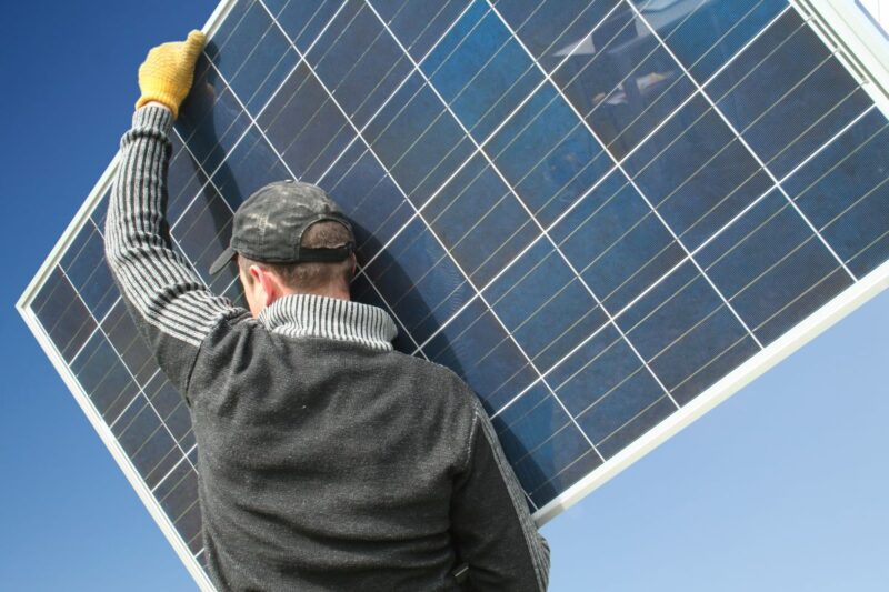 Mann, der Photovoltaik-Modul trägt - Symbol für Zusammenarbeit von Elektro- und Dachdecker-Handwerk