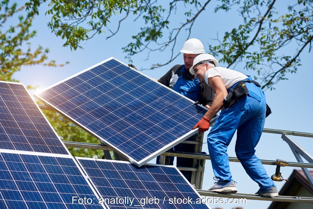 Zwei Monteure platzieren bei Sonnenschein ein Solarmodul auf ein Schrägdachgestell.