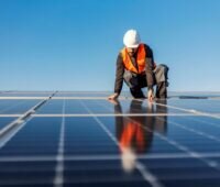 Arbeiter mit Schutzhelm und -weste auf Photovoltaikdach.