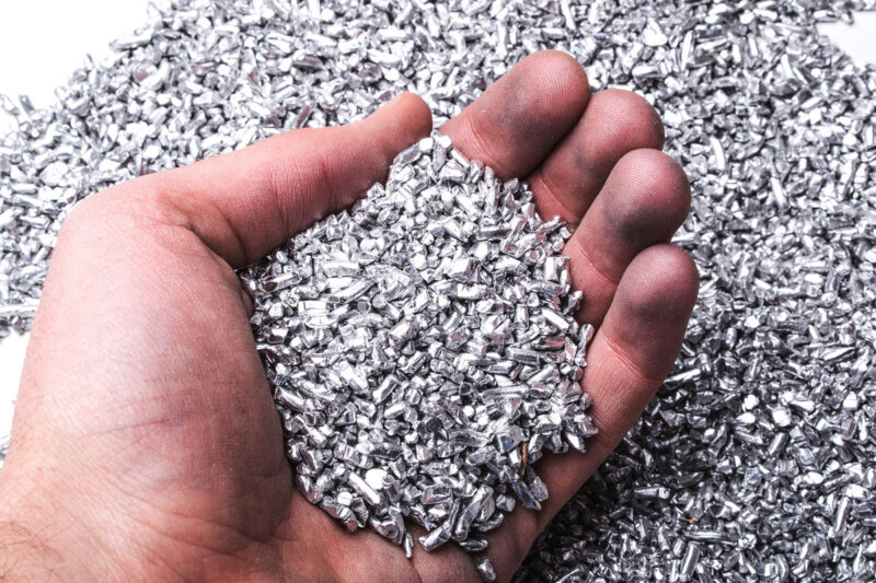 Silber- (oder Aluminium-)pellets in einer Hand. Symbolbild für Silber als wertvollen Rohstoff.