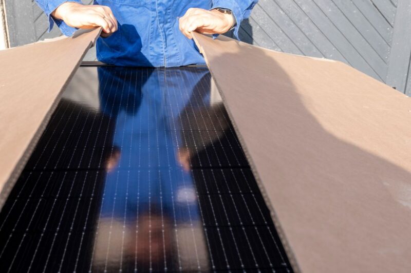 Person im Blaumann öffnet Paket mit Solarmodulen.