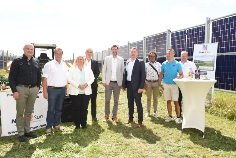 Menschengruppe neben senkrechten Solarmodulen.