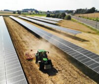 Ein Traktor zieht eine Egge durch eine Agri-PV-Anlage mit einem Tracker-System.