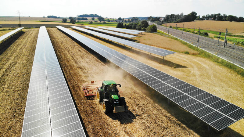 Ein Traktor zieht eine Egge durch eine Agri-PV-Anlage mit einem Tracker-System.