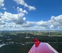 Blick über die Flügelspitze eines Flugzeugs auf einen Windpark unter blauem Himmel.