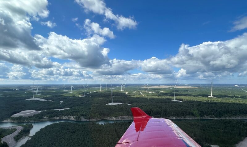 Blick über die Flügelspitze eines Flugzeugs auf einen Windpark unter blauem Himmel.