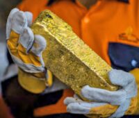 Minenarbeiter hält Goldbarren in den Handschuh-Händen.