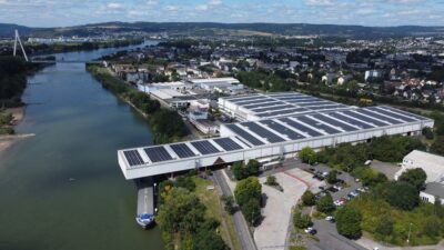 Luftaufnahme zeigt Betriebsgebäude an einem Fluß mit Photovoltaik auf den Dächern.