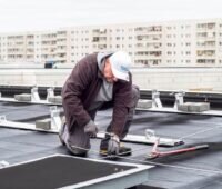 Ein Mann montiert auf einem Hochhausdach Bahnen für Solarmodule.
