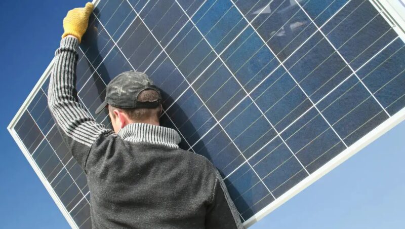 Im Bild ein Mann mit Solarmodul auf den Schultern als Symbol für den Photovoltaik-Bürokratieabbau.