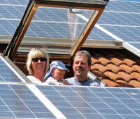 Zu sehen ist eine Familione, die aus dem Dachfenster ihres mit PV belegten Daches schaut. Ohne Solardeckel-Streichung, würde sich der Solarmarkt in Deutschland mehr als halbieren.