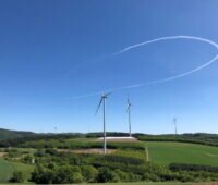 Windkraftanlagen auf welligem Terrain unter blauem Himmel.