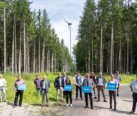 Zu sehen ist eine Menschengruppe mit Wirtschaftsminister Hubert Aiwanger im Wald vor einer Windenergieanlage bei der Auszeichnung „Gestalter der Energiewende“.