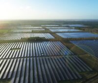 Luftbild eines raumgreifenden PV-Parks bei tiefstehender Sonne im Flachland.