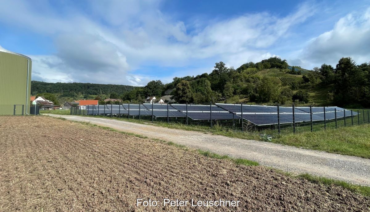 Solarkollektorfeld hinter Zäunen und neben einem Getreidespeicher.