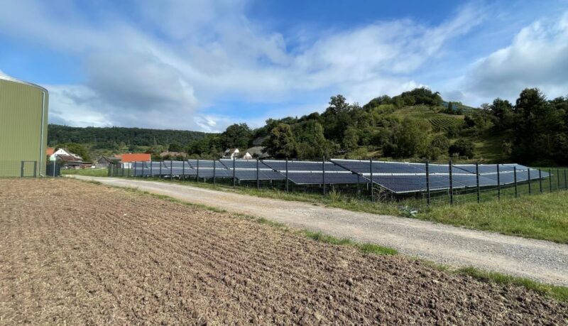 Solarkollektorfeld hinter Zäunen und neben einem Getreidespeicher.