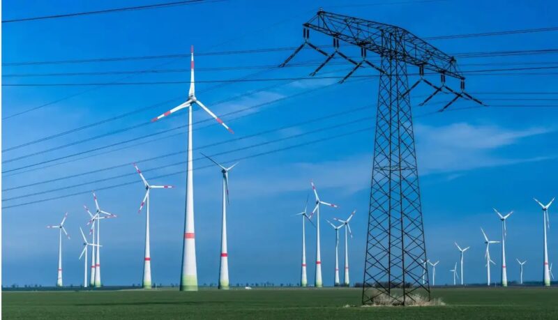 Windenergie-Anlagen und Strommast. Symbolbild für die Ausschreibung für Windenergie an Land.