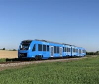 Ein blauer Zug fährt durch eine Frühlingslandschaft.