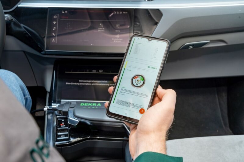 Hand hält Smartphone in einem Auto - Batterie-Schnelltest für Elektro-Autos bei der Dekra