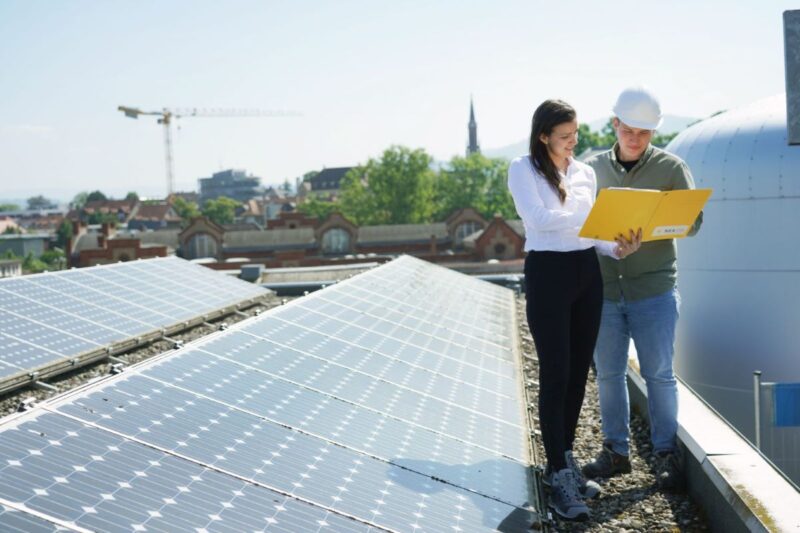 Eine Frau und ein Mann führen eine Besprechung durch auf einem DSach mit PV-Anlage.