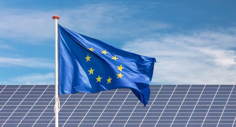 Im Bild eine Europaflagge vor Photovoltaik-Anlage als Symbol für die Europäische Solarakademie.
