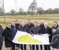 Im Bild 12 Offizielle mit Plan in den Händen, die den Messe-Parkplatz in Essen besuchen, auf dem der Solar-Carport entstehen soll.