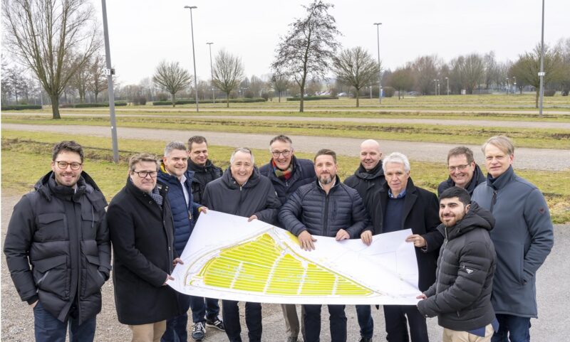 Im Bild 12 Offizielle mit Plan in den Händen, die den Messe-Parkplatz in Essen besuchen, auf dem der Solar-Carport entstehen soll.