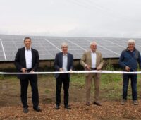 Vier Männer stehen vor einer Photovoltaik-Anlage und durchschneiden ein weißes Band.