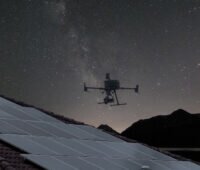 Drohne schwebt über Dach-PV-Anlage vor Sternenhimmel - Messung mit Elektrolumineszenz-Verfahren.