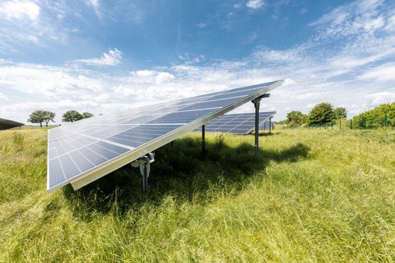 Freiflächensolarpark auf grüner Wiese unter blauem Himmel mit Wolken.