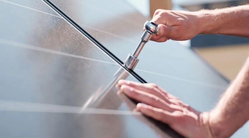 Im Bild eine Hand mit einer Ratsche, die ein Photovoltaik-Modul befestigt. Die EnWG-Novelle soll Hürden für Solarinstallationsunternehmen abbauen.