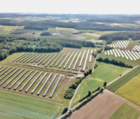 Luftbild einer Photovoltaik-Freiflächen-Anlage aus mehreren Teilfeldern zwischen Wiesen und Wäldern.