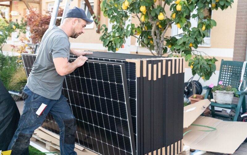 Im Bild ein Mann mit PV-Modulen, Enpal hat sich 5 Milliarden Euro Finanzierung gesichert.