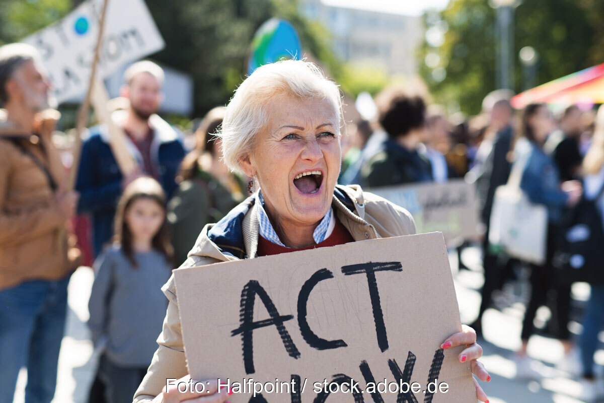 Frau mit Pappschild "Act now" - Symbol für Klimaklage der DUH gegen die Bundesregierung.